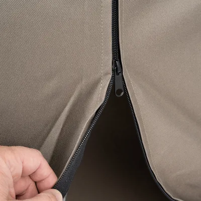 Close-up van een bruin stoffen materiaal met een zwarte ritssluiting die wordt geopend.