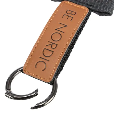 Étiquette en simili cuir avec texte BE NORDIC, anneau métallique visible, couture sur sangle textile noire.