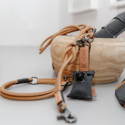 Laisse en corde beige avec mousqueton métal, étiquette BE NORDIC visible, pochette noire attachée, bol en bois en arrière-plan.