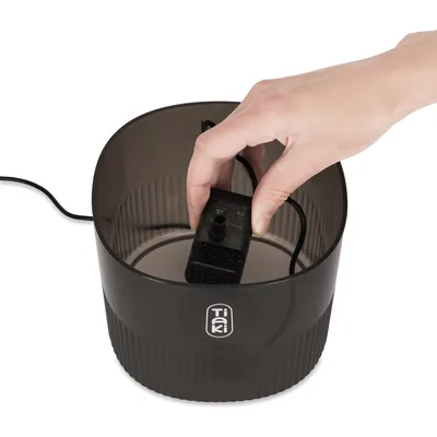Hand zeigt Installation einer Pumpe in einen schwarzen Tiki-Wasserspender.