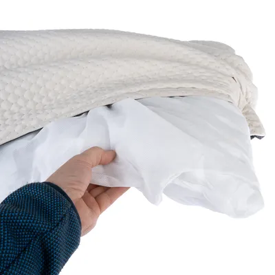 Hand zeigt die Schichten eines Kissens: weisse Netzschicht und beige gepolsterte Oberfläche mit Wabenmuster.