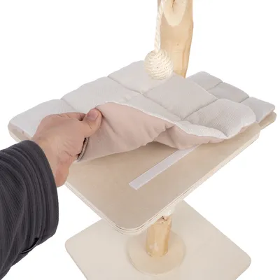 Abnehmbares, gepolstertes Kissen mit Klettverschluss auf einer Holzplattform eines Kratzbaums. Hand hebt das Kissen an.