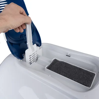 Hand zeigt die Entnahme einer weissen Streuschaufel aus einem Fach in einer Katzentoilette mit integriertem Aktivkohlefilter.