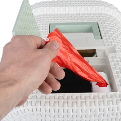 Hand zieht roten Müllbeutel aus einem weissen Behälter mit geflochtenem Design und integriertem Fach.