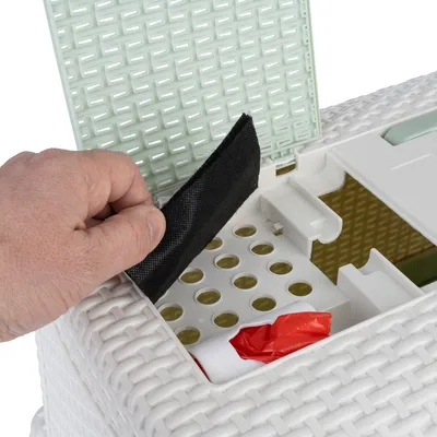 Hand öffnet Deckel einer weissen Box mit grünem Einsatz und zeigt Innenraum mit Filter, Löchern und rotem Beutel.