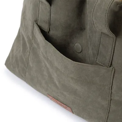 Vue rapprochée d’un sac en tissu avec une grande poche extérieure et une étiquette en cuir cousue sur le devant, bouton pression visible à l’intérieur de la poche.