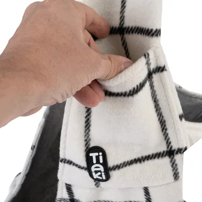 Main glissant dans une poche sur un tissu à carreaux blancs et noirs avec l’étiquette Tiaki visible. Matière polaire.