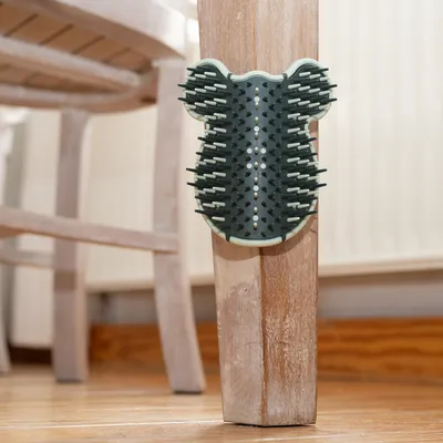 Scratching brush shaped like a bear's head, attached to a wooden chair leg. Dark green bristles with visible white accents.
