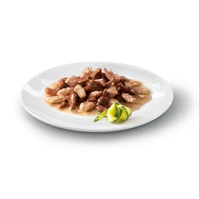 Serveringsförslag: köttbitar i sås på vit tallrik, dekorerad med zucchinistrimlor och örter.