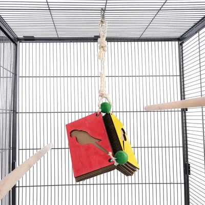 Hängendes Spielzeug aus Pappe mit roten und gelben Elementen, Papageien-Silhouetten und grünen Holzkugeln in einem Vogelkäfig.