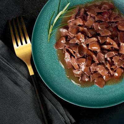 Chunks of meat in gravy served on a green plate with a sprig of rosemary, shown close up for product detail.