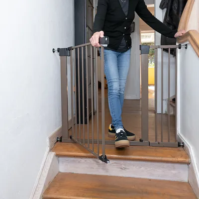 Person öppnar en brun säkerhetsgrind av metall som är installerad högst upp i en trappa.
