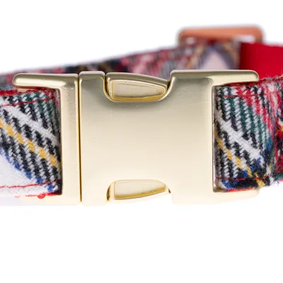 Gros plan sur la boucle en métal doré d’un collier à motif écossais en tissu, détails visibles du fermoir et des coutures.