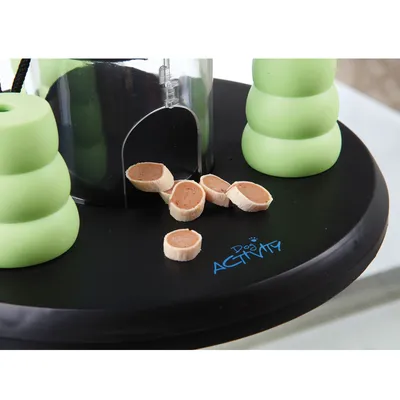 Играчка за кучета Dog Activity с черна основа, зелени елементи и лакомства, изсипани пред прозрачен контейнер.