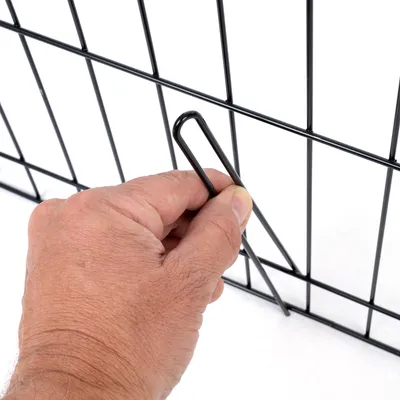 Main tenant une tige métallique pour fixer un panneau de grille en métal noir, détail du système d’assemblage visible.