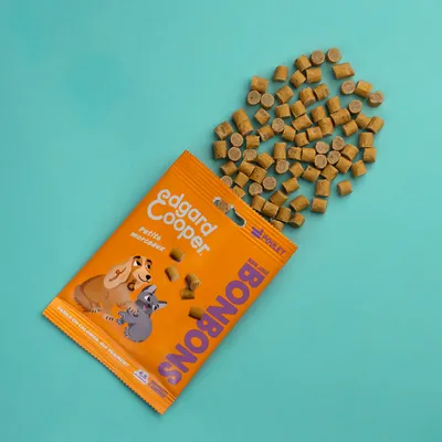 Edgard Cooper Bonbons, petits morceaux, emballage orange avec chien et chat, friandises dispersées sur fond bleu.