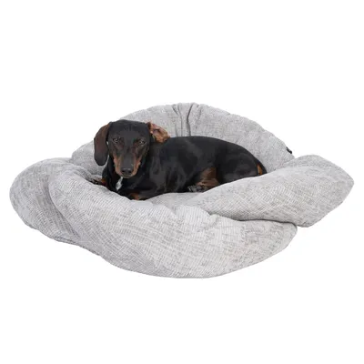 Chien noir allongé sur un grand coussin rond gris en tissu, sans marque visible. Le coussin a une texture tissée et des bords épais rembourrés.