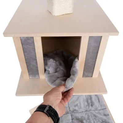 Mano muestra un cojín gris extraíble de una cueva de madera con superficie rascadora de sisal en la parte superior y tiras de fieltro gris en los laterales.