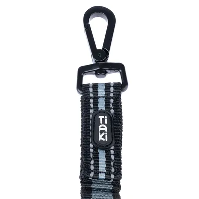 Czarny karabińczyk z odblaskowym paskiem i logo Tiaki na czarnej taśmie nylonowej.