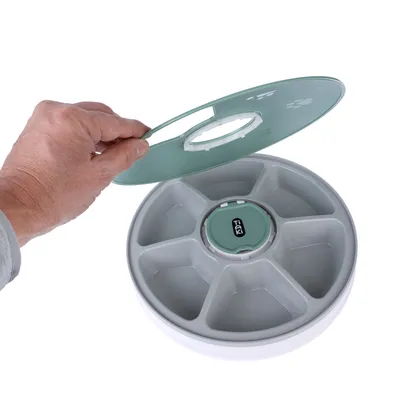 Round feeding station with six numbered compartments and removable lid, brand Trixi. Hand shows lid opening.