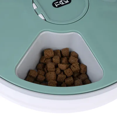 Food dispenser with green lid and compartment filled with brown dry food cubes.