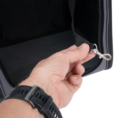 Hand toont een karabijnhaak aan een zwarte riem die aan een tas is bevestigd.