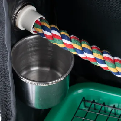 Gamelle en métal fixée à une cage, corde tressée multicolore et bac vert avec grille visibles à l’intérieur.