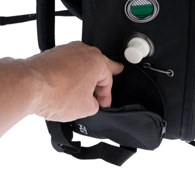 Main ouvrant une poche zippée sur un sac noir avec œillets métalliques et bouton blanc visibles. Étiquette partiellement lisible : 'T...Y'.