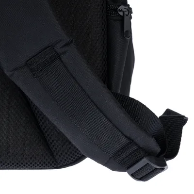 Gros plan sur une sangle réglable en tissu noir avec boucle plastique et dos matelassé d’un sac, fermeture éclair visible.