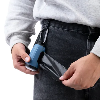 Person zieht eine schwarze Hundekotbeutel aus einem blauen Spender, der an einer Gürtelschlaufe befestigt ist.