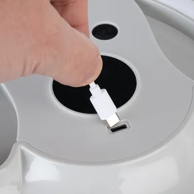 Hand steckt ein USB-C-Kabel in die Ladebuchse eines grauen Geräts mit einem schwarzen Ein-/Ausschalter.