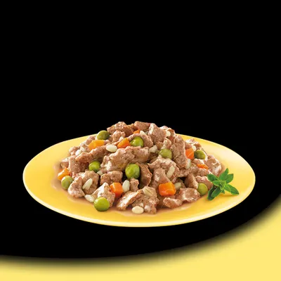 Piatto giallo con bocconcini di carne in salsa, piselli verdi, carote a cubetti e semi visibili, decorato con una foglia verde.