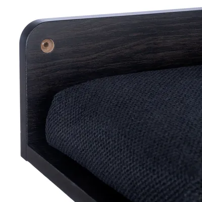 Détail d’un lit pour animal avec structure en bois foncé et coussin en tissu noir à texture visible.
