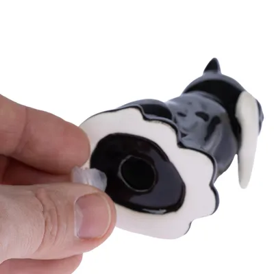 Jouet en forme de chien noir et blanc tenu par une main, ouverture visible à la base avec bouchon en plastique transparent. Matière : plastique.