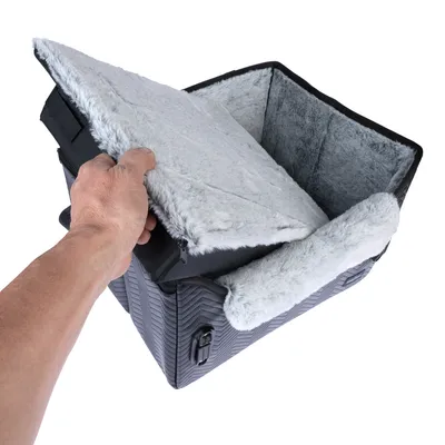 Hand öffnet eine graue Transporttasche mit weichem, abnehmbarem Innenfutter aus Plüsch und Reissverschluss. Tasche hat ein strukturiertes Design und einen Verschlussclip.