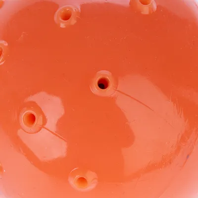Balle orange en plastique avec plusieurs trous visibles à la surface, vue rapprochée du jouet sans marque ni texte apparent.