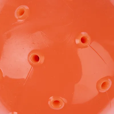 Gros plan sur une surface orange en plastique avec plusieurs trous ronds visibles, sans marque ni texte apparent.