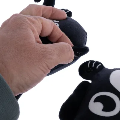 Kéz kinyitja a tépőzárat egy fekete plüssjátékon fehér részletekkel.