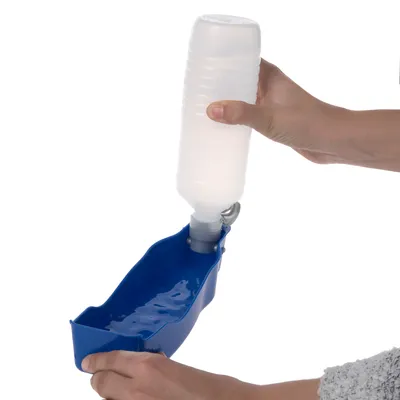 Hand hält eine weisse Wasserflasche, die in eine blaue tragbare Trinkschale für Haustiere eingefüllt wird.