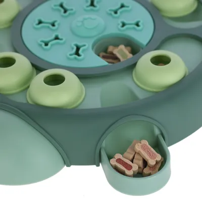 Jeu interactif vert pour chien avec compartiments et friandises en forme d’os visibles dans un tiroir ouvert et sous une trappe coulissante. Matière plastique.