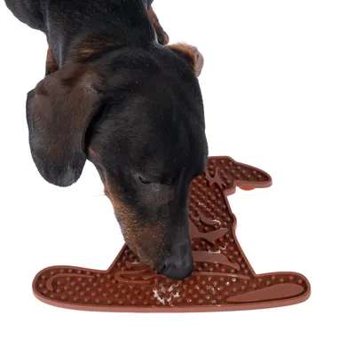 Hund leckt Futter von einer braunen Silikonmatte in Form eines Hundekopfes mit strukturierten Oberflächen.