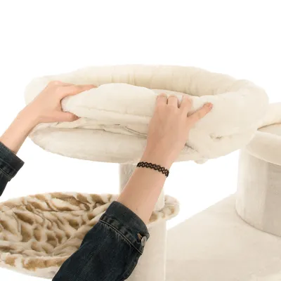 Handen plaatsen een afneembare, zachte witte pluche mand op een krabpaal voor katten. Onder de mand is een ligplateau met dierenprint zichtbaar.