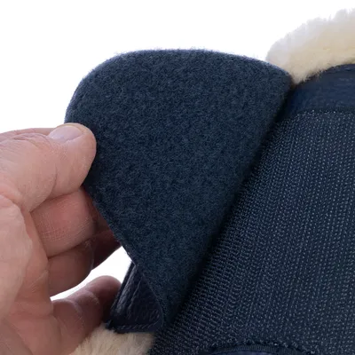 Gros plan sur une main soulevant une fermeture velcro noire d’un accessoire en tissu avec doublure intérieure beige visible.