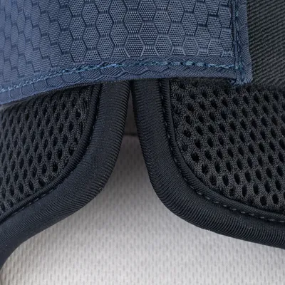 Gros plan sur des matériaux textiles : tissu bleu à motif hexagonal et maille noire respirante, coutures visibles. Aucun logo ou texte apparent.