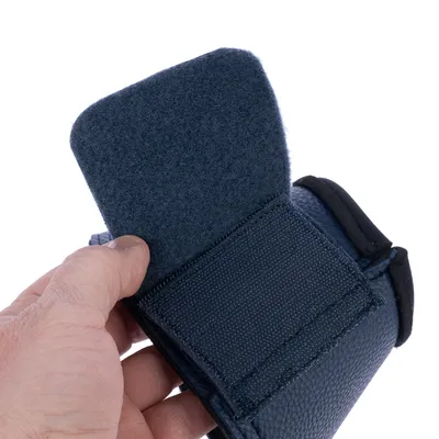 Nahaufnahme einer Hand, die eine dunkelblaue Klettverschlusslasche öffnet. Zeigt Materialstruktur und Funktion des Verschlusses.