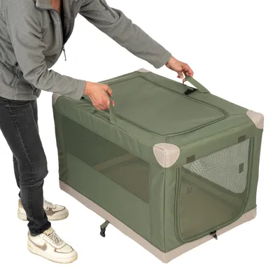 Caja de transporte verde con ventanas de malla y asas de transporte, levantada por una persona. Esquinas con tela reforzada.