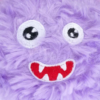 Jouet en peluche violette avec yeux brodés noirs et blancs, bouche rouge à dents blanches brodées, texture duveteuse visible.