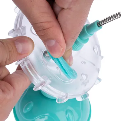 Ruka pokazuje umetanje zelenog plastičnog klipa u prozirni uređaj. Prikaz montaže igračke ili dodatka.