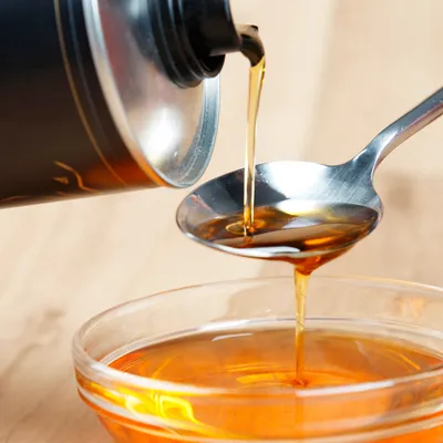 Flüssigkeit aus einer schwarzen Flasche wird in einen Löffel gegossen, darunter eine Glasschale mit derselben Flüssigkeit.
