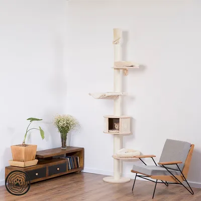 Tiragraffi beige a soffitto con più piattaforme e cuccia, posizionato in un angolo di soggiorno moderno. Un gatto visibile nella cuccia centrale.